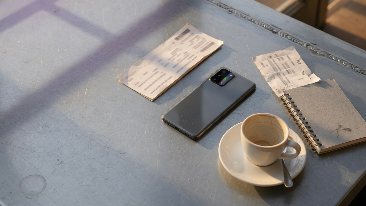A grey phone lying face down on a scratched zinc cafe table beside a torn boarding pass stub, a grey spiral notebook and a white espresso cup, in low warm afternoon sunlight