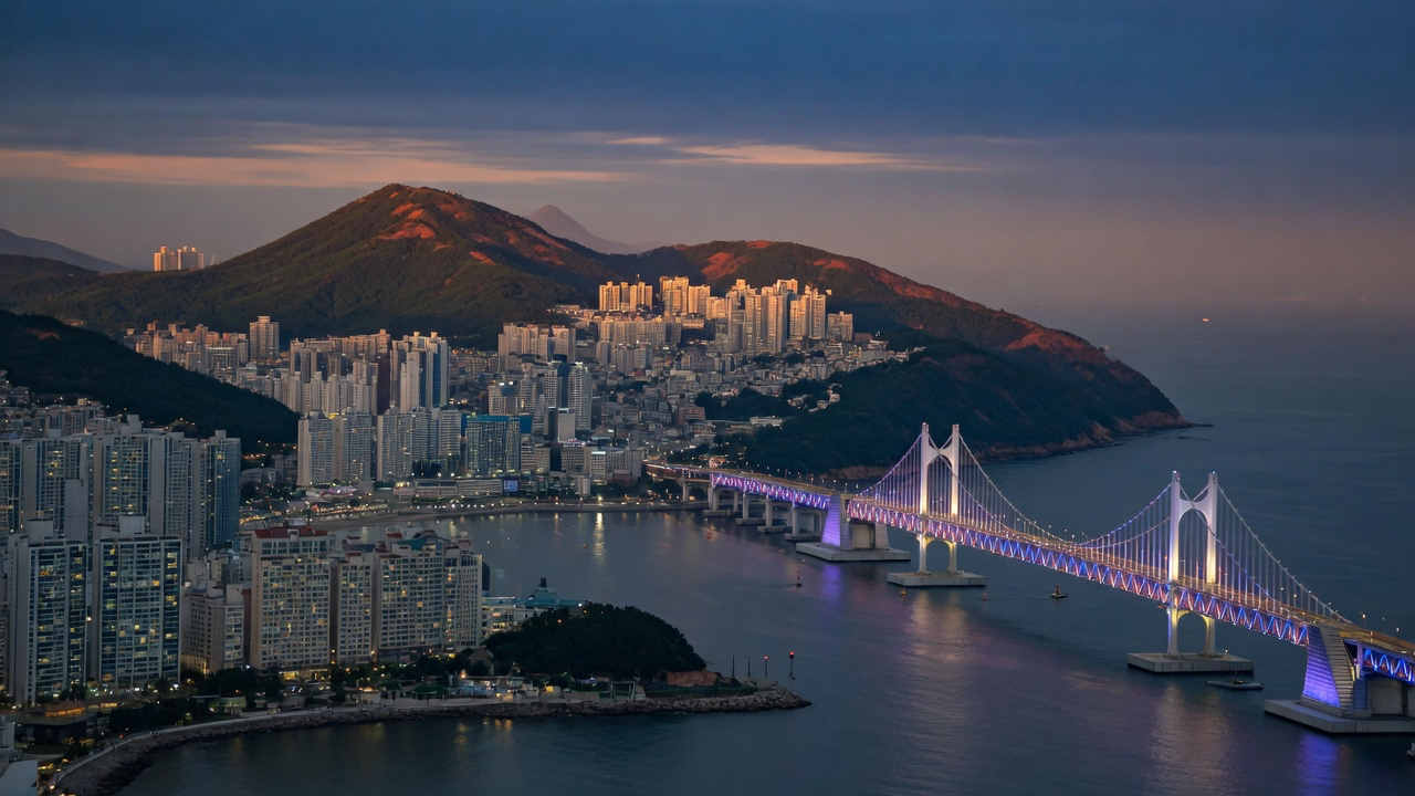 Busan at dusk, hillside apartment towers around the bay and the lit Gwangan Bridge