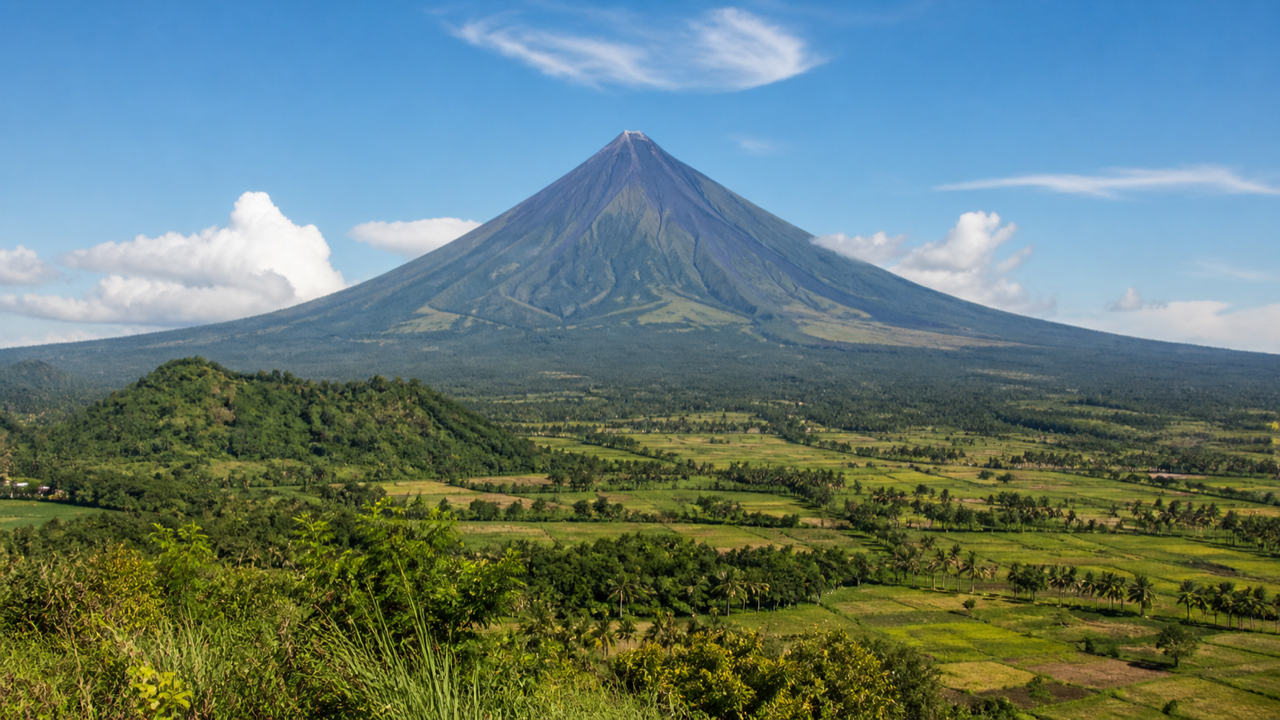 Mayon Volcano's symmetrical cone rising above green fields under a clear sky